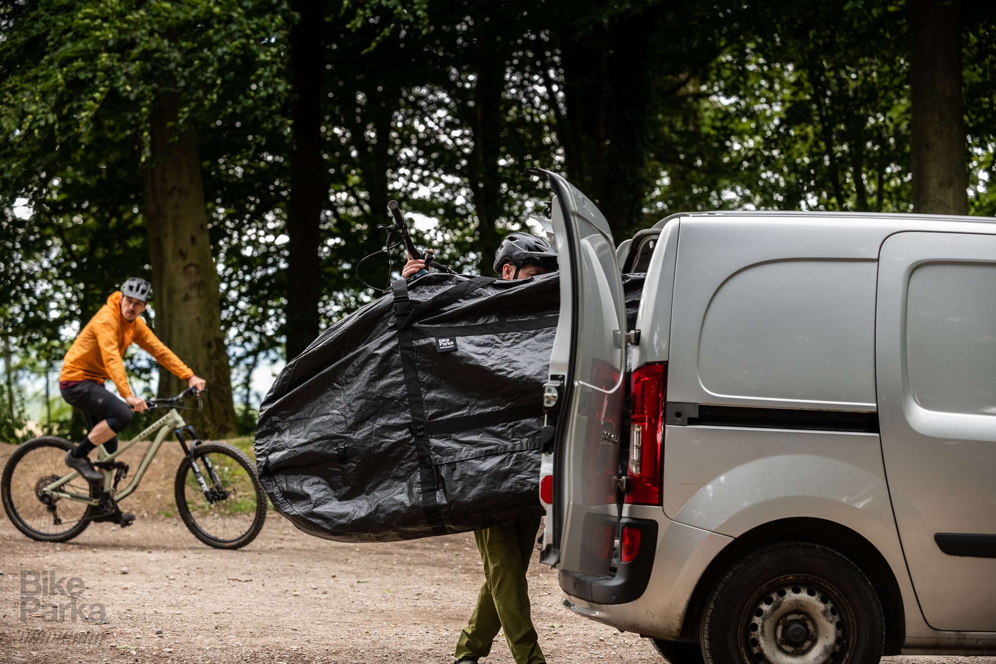 Cyclist packing muddy bike into BikeParka RoughSac for transport in van